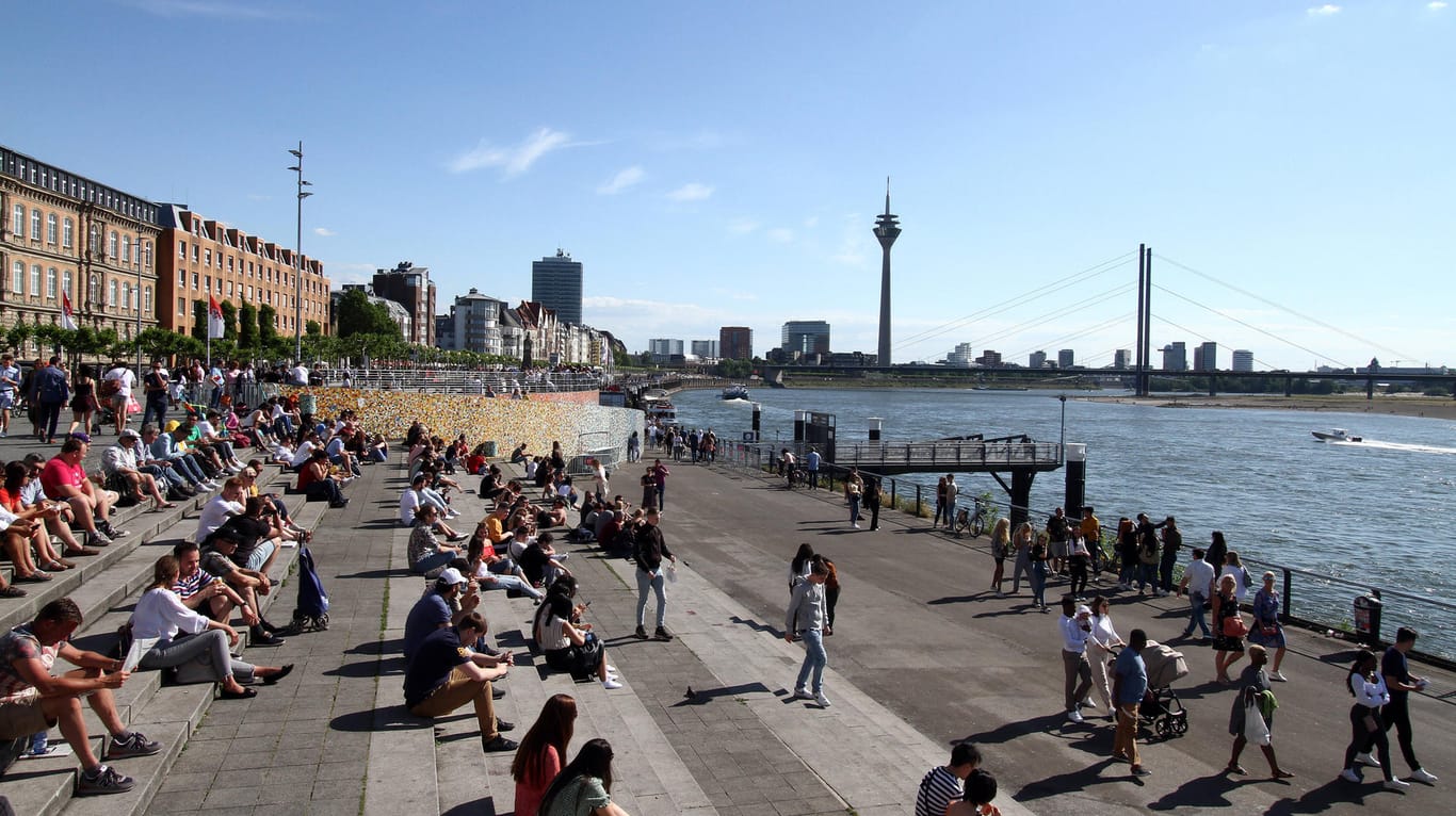 Menschen in Düsseldorf genießen die Sonne am Rheinufer: Zu Beginn der Woche wird es nochmal richtig warm – danach ist es mit dem Sonnenbaden wohl erstmal vorbei.