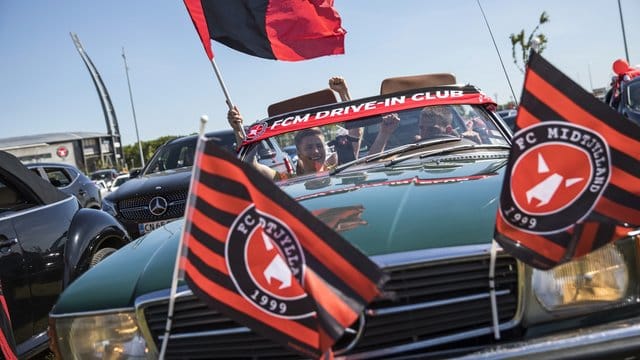 Fußballfans verfolgen das Spiel zwischen dem FC Midtjylland und dem AC Horsens auf dem Parkplatz vor dem Stadion.