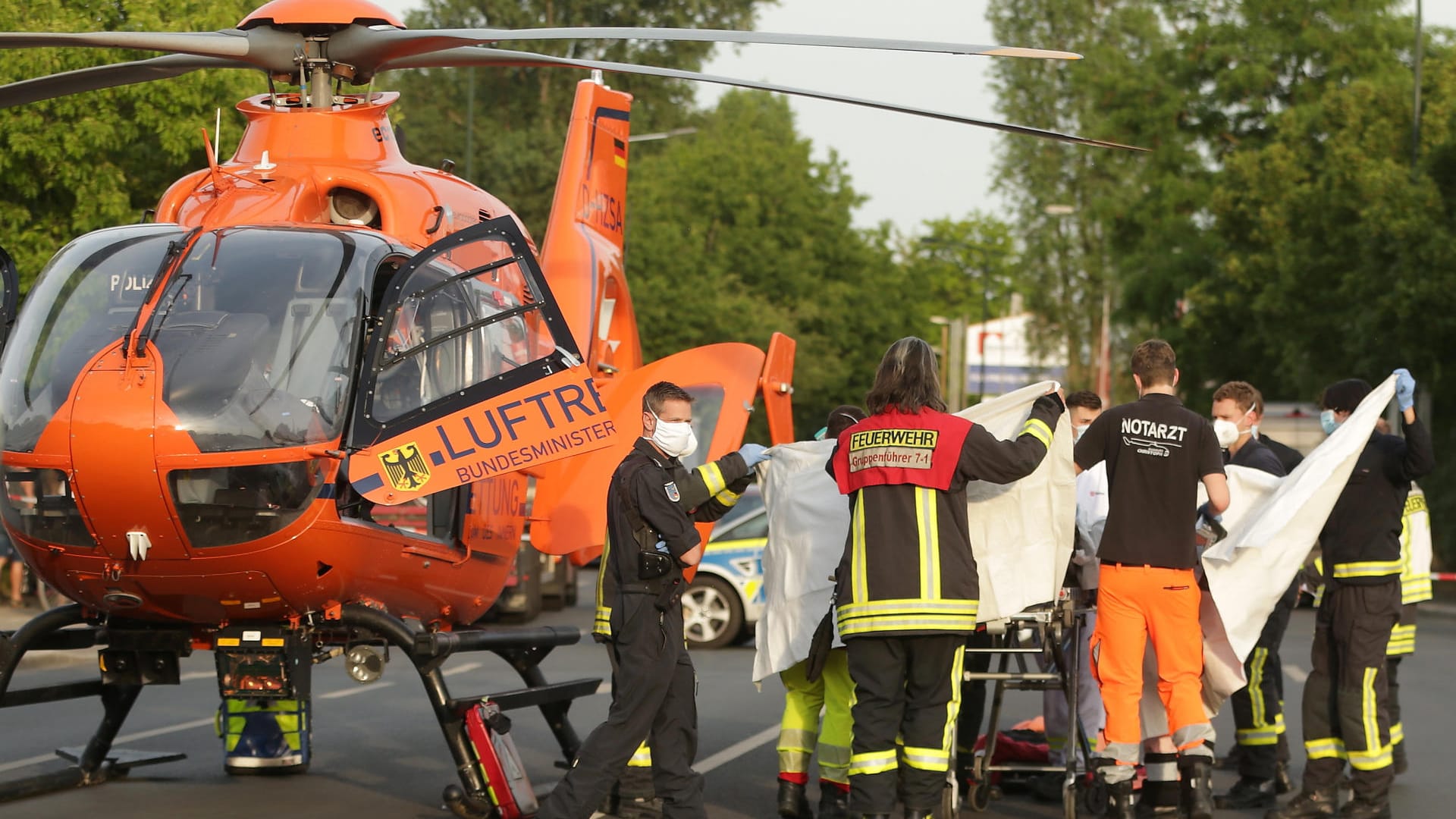Rettungskräfte bringen eine verletzte Person zu einem Rettungshubschrauber, der in der Nähe einer Bushaltestelle auf der Straße steht: In Düsseldorf hat ein Mensch Feuer gefangen. Rettungskräfte bringen eine verletzte Person zu einem Rettungshubschrauber, der in der Nähe einer Bushaltestelle auf der Straße steht: In Düsseldorf hat ein Mensch Feuer gefangen.
