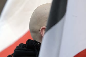 En Mann mit geschorenem Kopf zwischen schwarz-weiß-roten Fahnen: Momentaufnahme einer Demo.