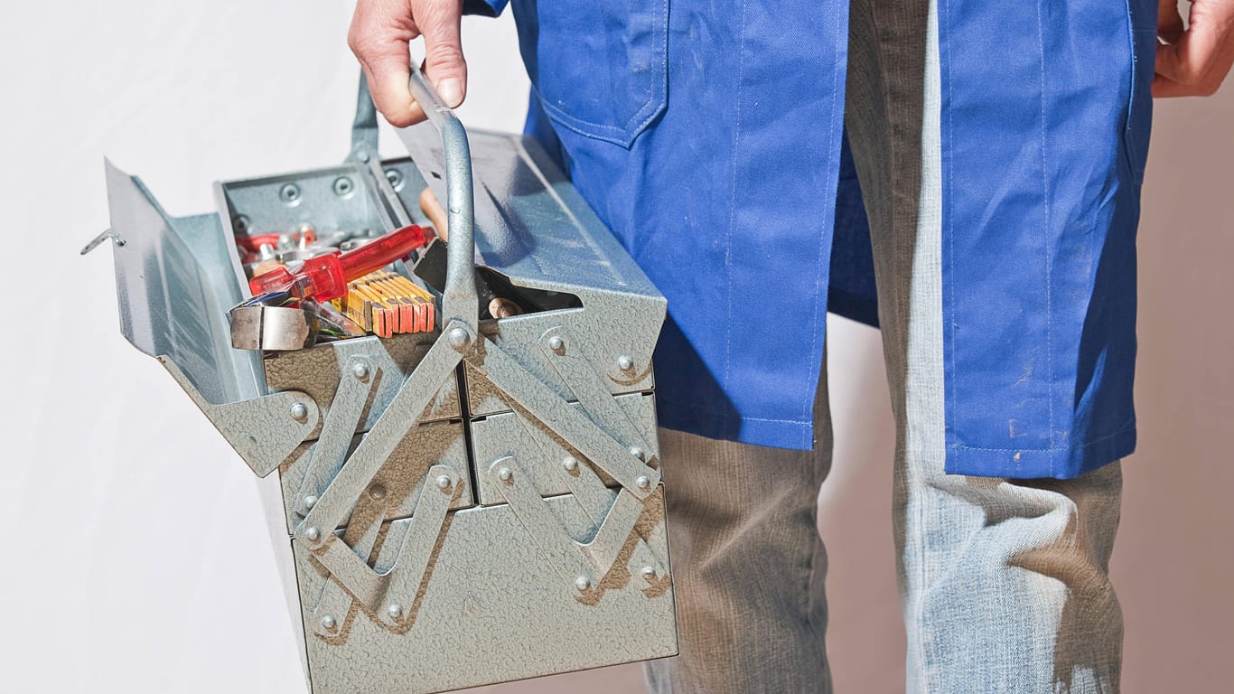 Eine Person im blauen Kittel trägt einen Werkzeugkasten: Ein falscher Handwerker soll wiederholt eine Seniorin überfallen haben.