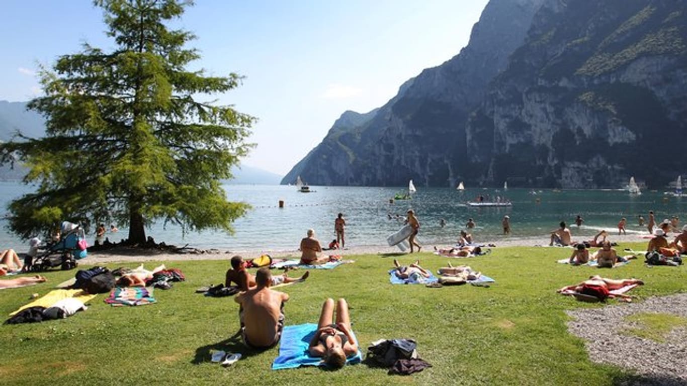 Touristen und Einheimische nehmen am Strand von Riva del Garda ein Sonnenbad.