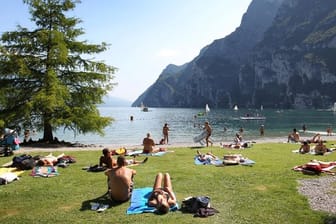 Touristen und Einheimische nehmen am Strand von Riva del Garda ein Sonnenbad.