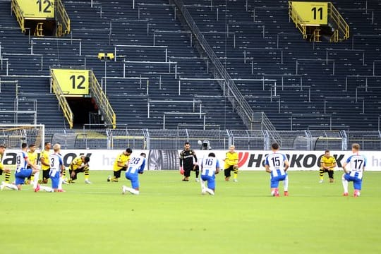 Spieler beider Mannschaften knien vor dem Anpfiff um den Mittelkreis und schweigen ein paar Minuten.