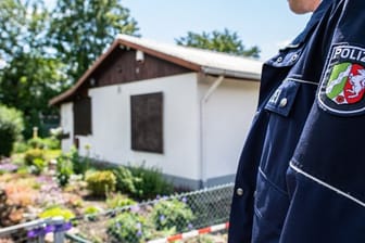 Ein Polizeibeamter steht vor der Gartenlaube in Münster, wo der vermutliche Haupttäter Teile seiner Server-Anlage unterbrachte.