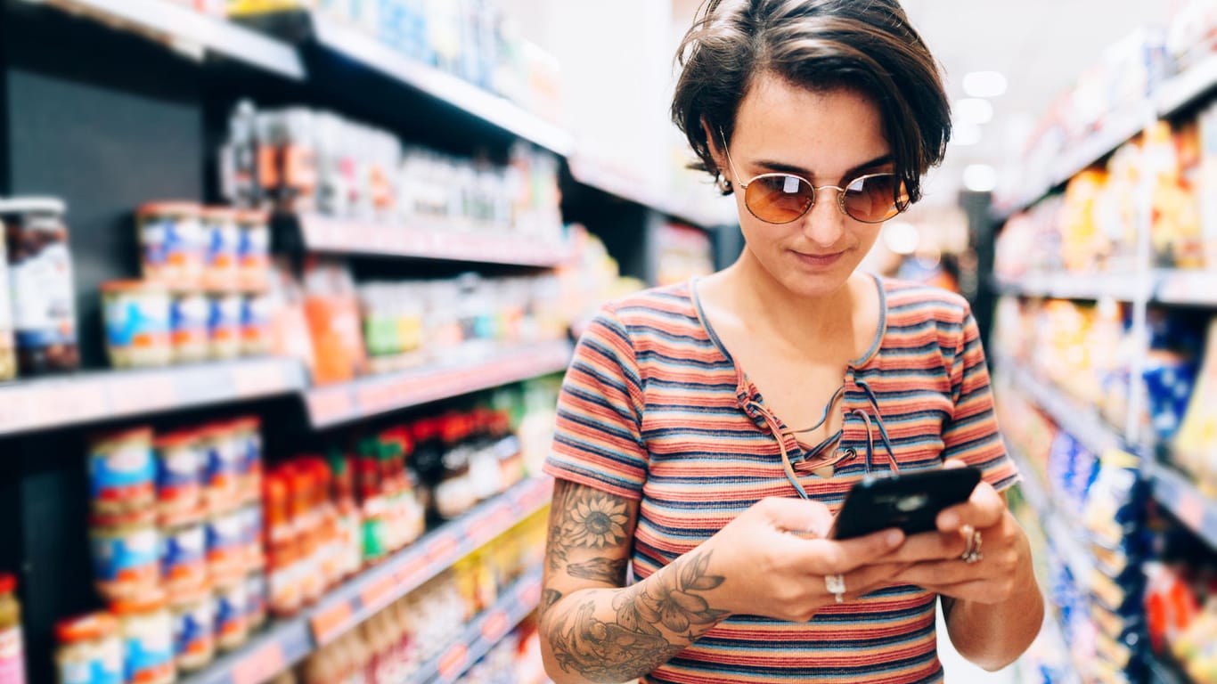 Ein Frau schaut im Supermarkt auf ihr Handy: Auch Lidl bietet seinen Kunden jetzt kostenloses WLAN an.
