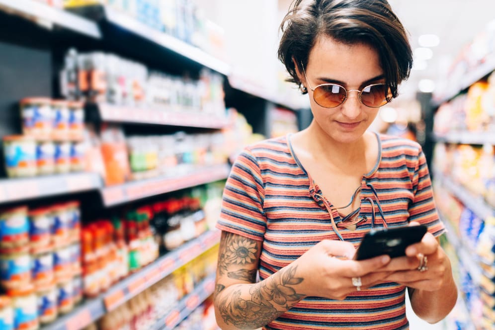 Ein Frau schaut im Supermarkt auf ihr Handy: Auch Lidl bietet seinen Kunden jetzt kostenloses WLAN an.