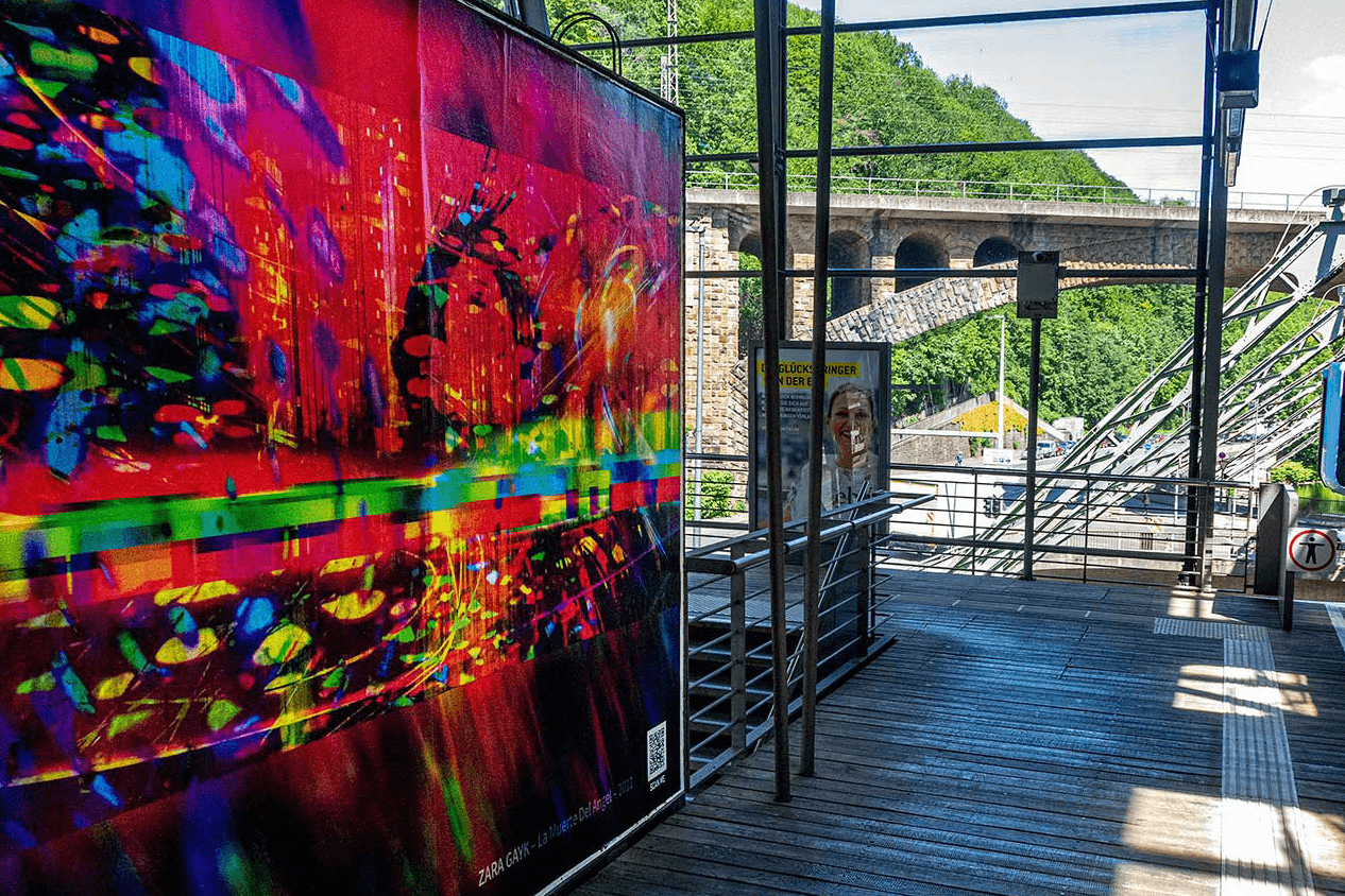 Ein Plakat des Künstlers Zara Gayk hängt an der Schwebebahnstation am Zoo/Stadion in Wuppertal: Über 150 solcher Motive sind in der ganzen Stadt zu sehen.