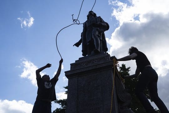 Zwei Männer befestigen ein Seil um den Hals einer Statue von Christopher Columbus.