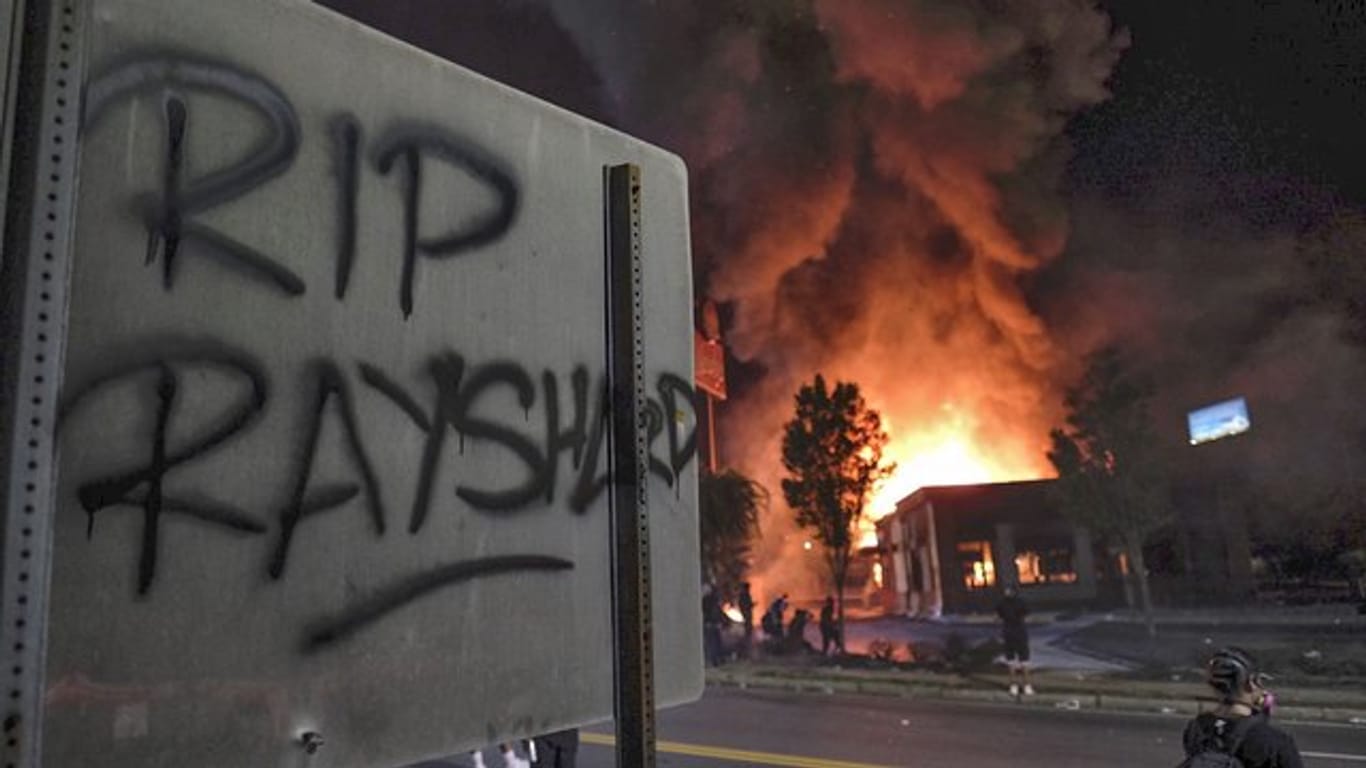 "RIP Rayshard" steht auf einem Schild, während im Hintergrund ein Wendy's-Restaurant brennt.