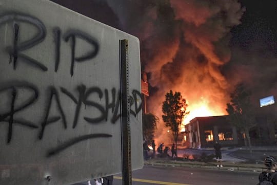 "RIP Rayshard" steht auf einem Schild, während im Hintergrund ein Wendy's-Restaurant brennt.