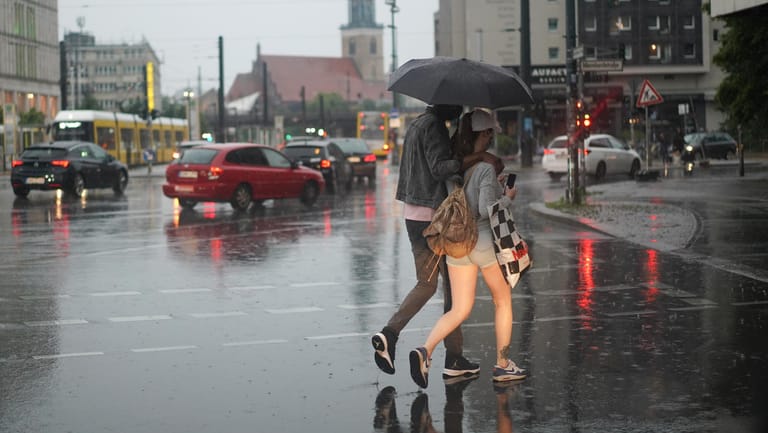 Berlin: Ein Paar überquert bei starkem Regen eine Straße.