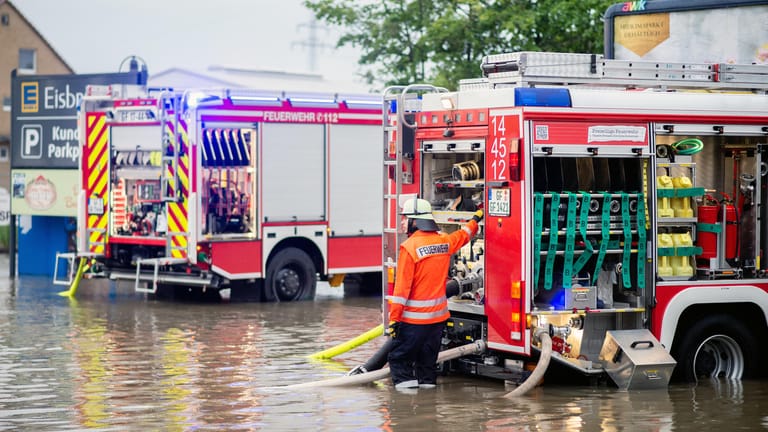 Niedersachsen: Zwei Einsatzfahrzeuge der Feuerwehr stehen auf dem überschwemmten Parkplatz eines Supermarktes im Landkreis Gifhorn, der durch Starkregen überflutet wurde und abgepumpt werden muss.