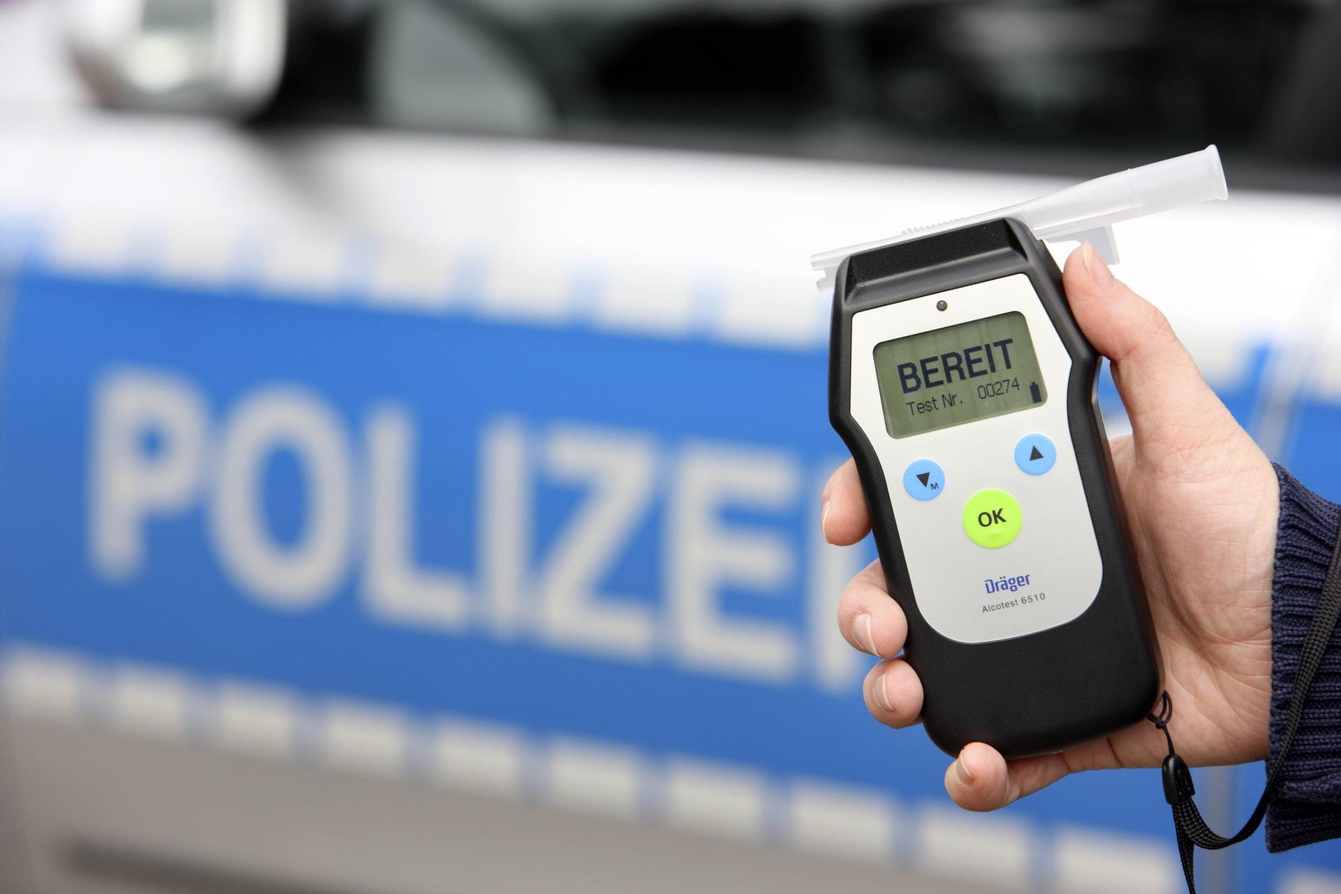 Eine Hand hält ein Atemalkohol-Testgerät vor einem Polizeiwagen (Symbolbild): In Hagen haben Polizisten einen betrunkenen Autofahrer ohne Führerschein gestoppt.