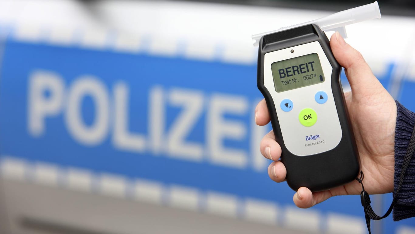 Eine Hand hält ein Atemalkohol-Testgerät vor einem Polizeiwagen (Symbolbild): In Hagen haben Polizisten einen betrunkenen Autofahrer ohne Führerschein gestoppt.