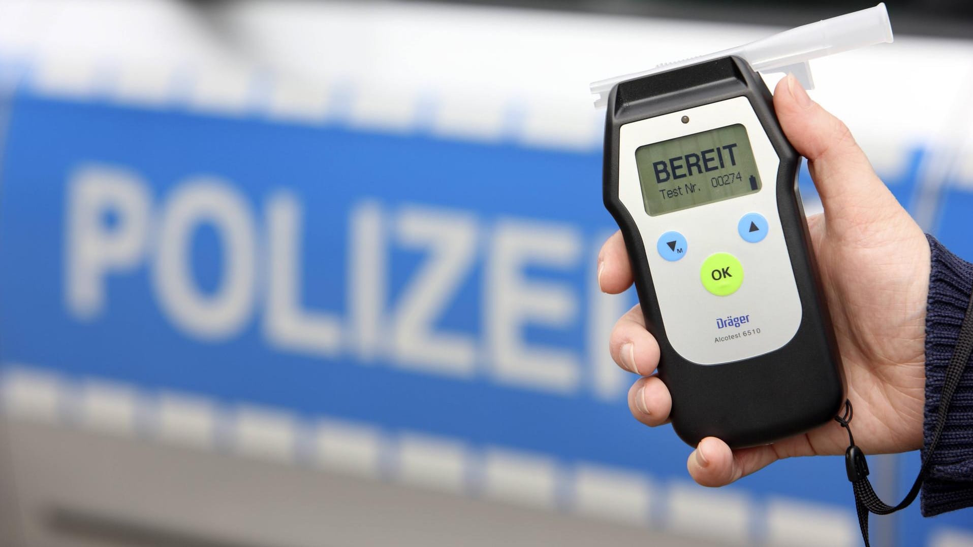 Eine Hand hält ein Atemalkohol-Testgerät vor einem Polizeiwagen (Symbolbild): In Hagen haben Polizisten einen betrunkenen Autofahrer ohne Führerschein gestoppt.