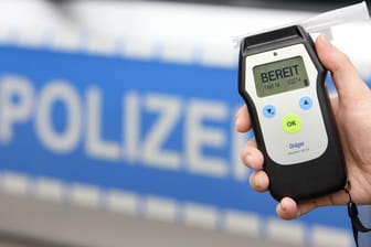 Eine Hand hält ein Atemalkohol-Testgerät vor einem Polizeiwagen (Symbolbild): In Hagen haben Polizisten einen betrunkenen Autofahrer ohne Führerschein gestoppt.