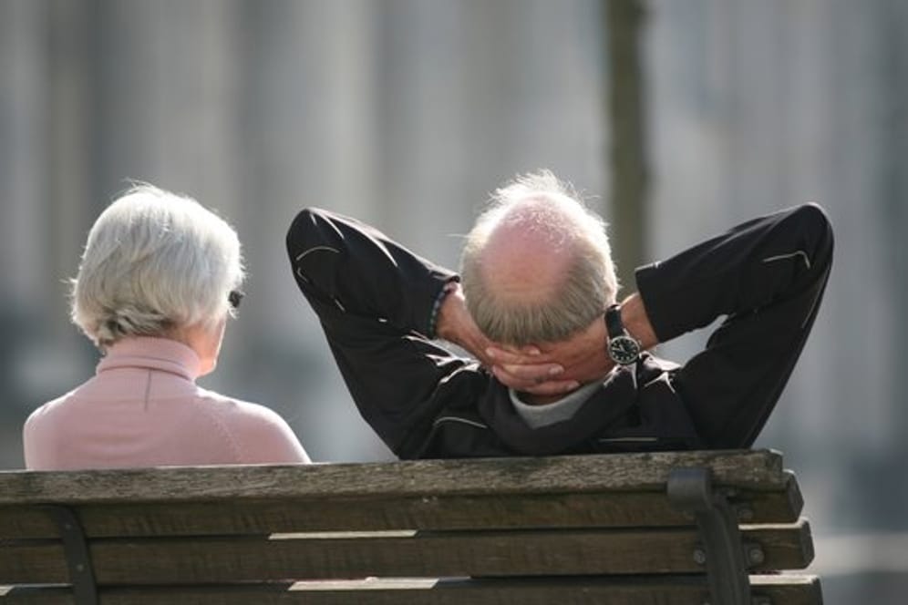 Ein Rentnerpaar sitzt auf einer Bank und sonnt sich.