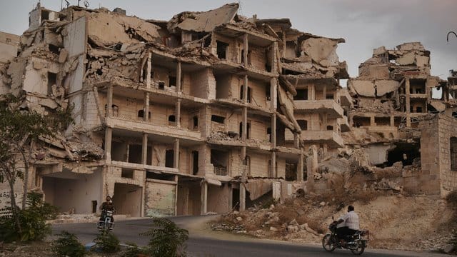 Motorradfahrer passieren zerstörte Gebäude in der Provinz Idlib.