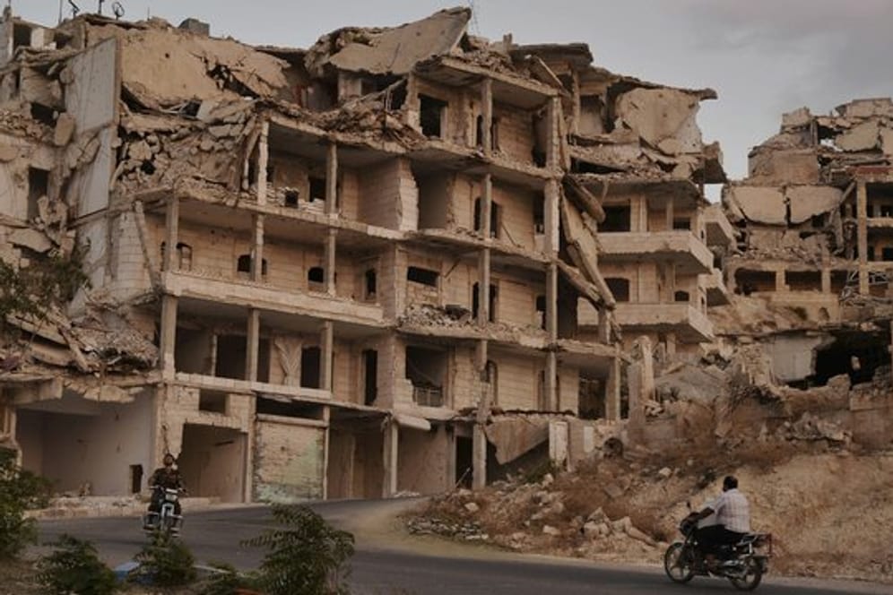 Motorradfahrer passieren zerstörte Gebäude in der Provinz Idlib.
