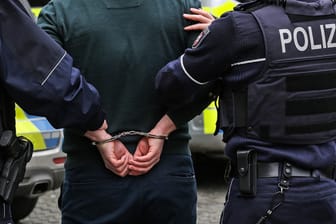 Zwei Polizisten mit einer Person in Handschellen (Symbolbild): Der Tatverdächtige in Hagen war wohl nur wegen einer verstrichenen Frist auf freiem Fuß.