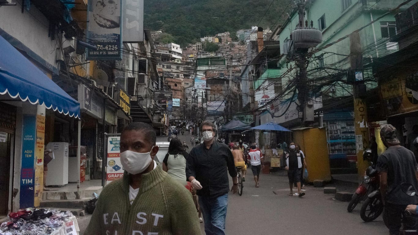 Rio De Janeiro: Menschen gehen mit Mundschutz durch eine Straße der Favela "Rocinha".