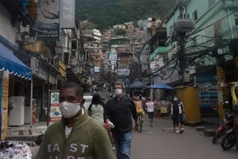 Rio De Janeiro: Menschen gehen mit Mundschutz durch eine Straße der Favela "Rocinha".