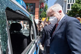 Bundesinnenminister Horst Seehofer (CSU) betrachtet während seines Besuchs ein Polizeiauto, das während der nächtlichen Randale beschädigt wurde.