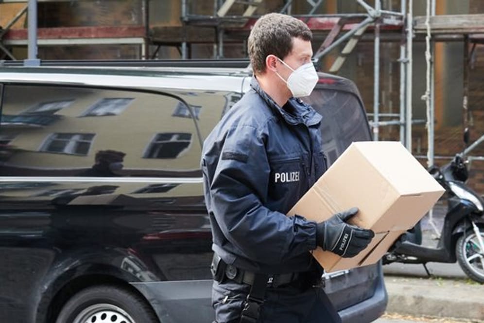 Ein Polizist trägt sichergestelltes Beweismaterial zu einem Auto.