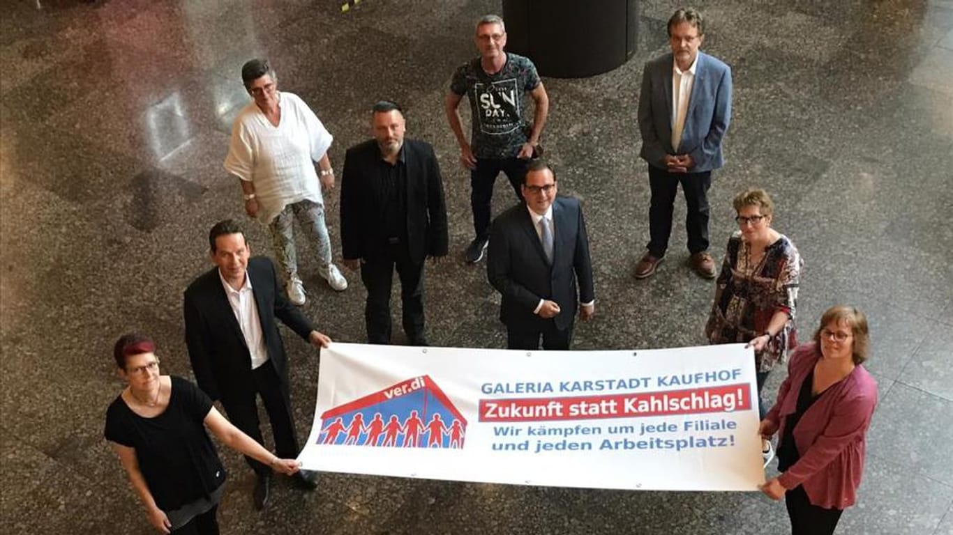 Vertreter der Stadt Essen, der Betriebsräte und Gewerkschaften halten ein Plakat: Gemeinsam wollen sie sich für den Erhalt der Karstadt-Kaufhof-Filialen einsetzen.