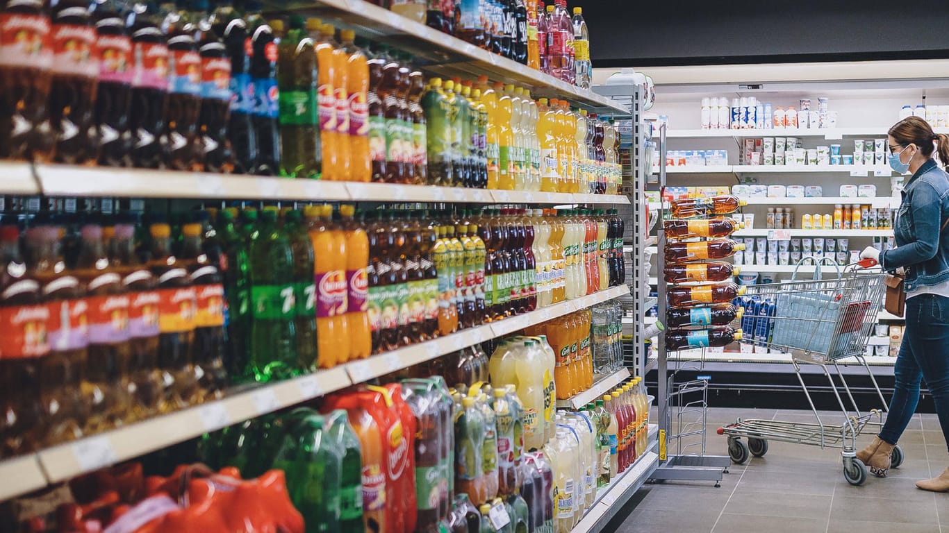 Eine Frau geht mit einem Einkaufswagen an dem Getränkeregal eines Supermarktes vorbei (Symbolbild): In München hat eine 56-Jährige Flaschen manipuliert und Getränke vergiftet.
