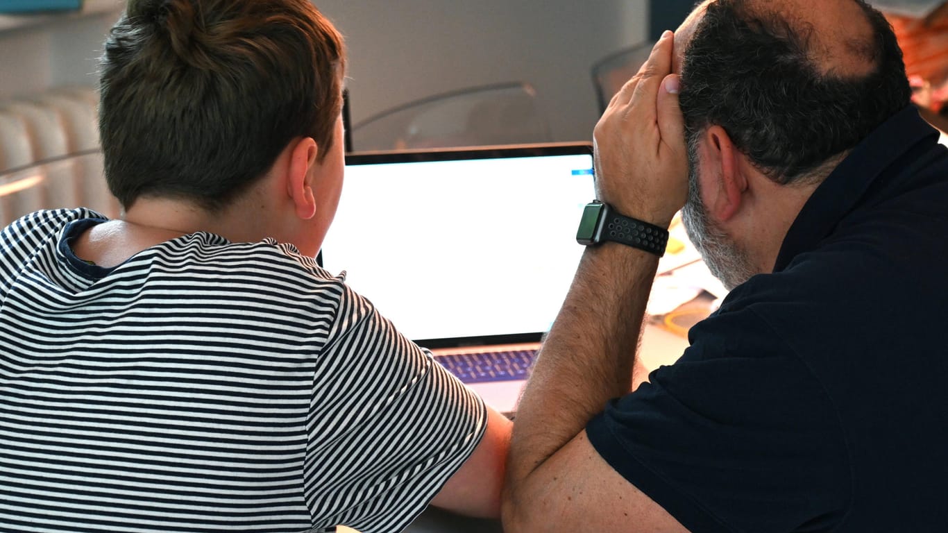 Vater und Sohn sitzen gemeinsam vor einem Laptop (Symbolbild): Zum Beispiel wegen fehlender Technik stellt das Homeschooling viele Familien vor Herausforderungen.