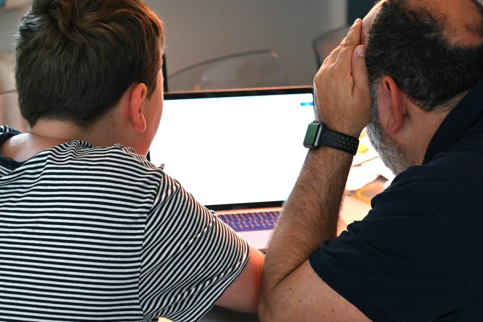 Vater und Sohn sitzen gemeinsam vor einem Laptop (Symbolbild): Zum Beispiel wegen fehlender Technik stellt das Homeschooling viele Familien vor Herausforderungen.