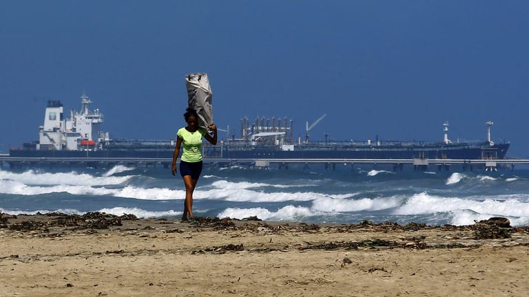 Frau am Strand von Puerto Cabello, Venezuela: Im Hintergrund ist der Öltanker Teseo zu sehen, der wegen US-Sanktionen nicht ablegt.