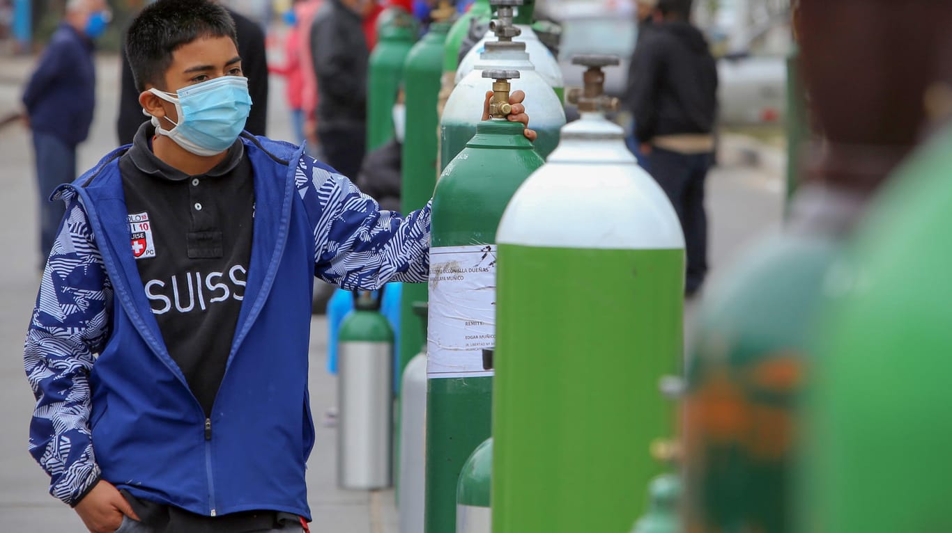 Der Peruaner Luis Gustavo Laupa Neira steht mit Mundschutz neben einer Sauerstoffflasche vor einem Laden, in dem die Flasche nachgefüllt werden soll.