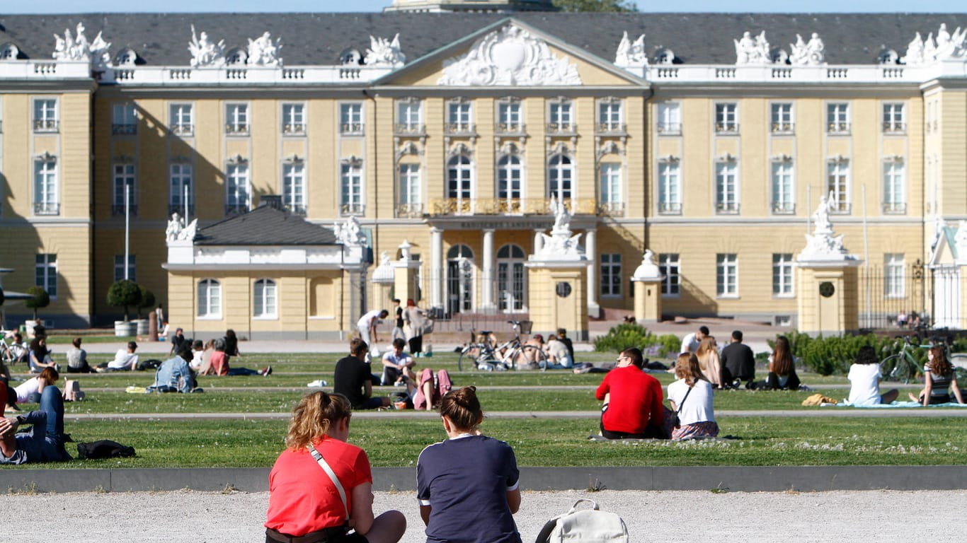 Personen sitzen auf den Rasenflächen am Schlossplatz: An diesem Ort kam es zu einem Angriff auf zwei Personen durch eine Gruppe.