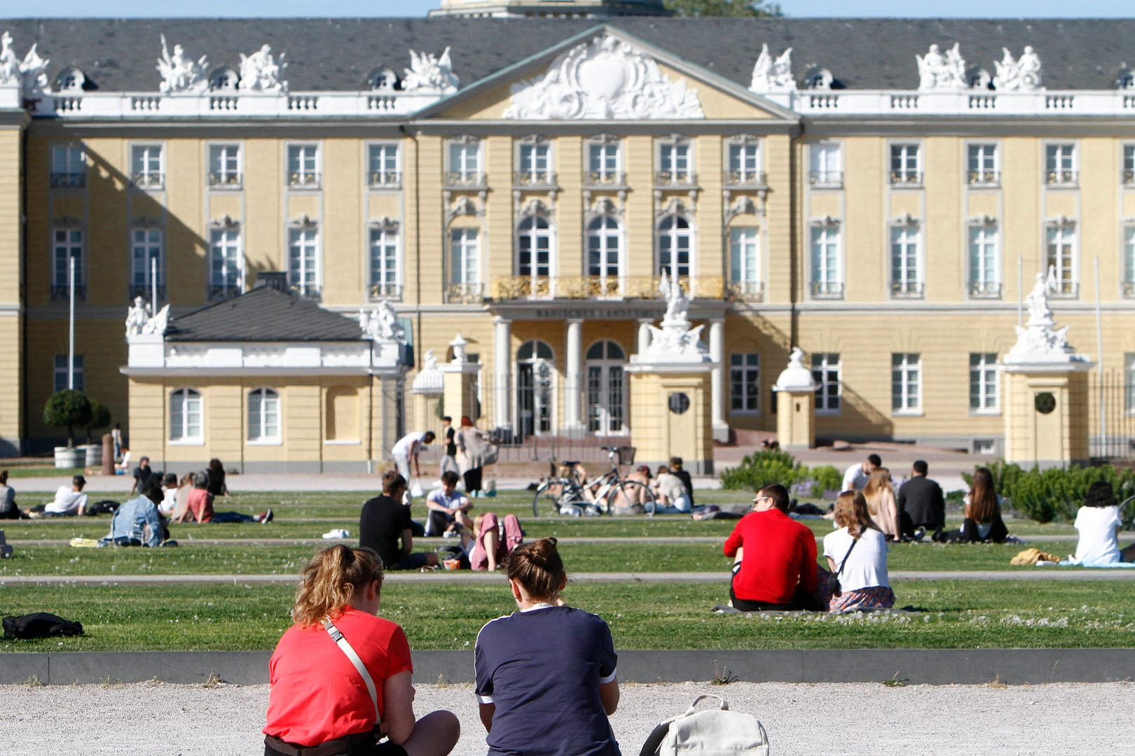 Personen sitzen auf den Rasenflächen am Schlossplatz: An diesem Ort kam es zu einem Angriff auf zwei Personen durch eine Gruppe.