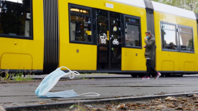 Eine Maske liegt auf dem Boden, dahinter fährt eine Tram: Nur jeder Vierte trägt bei der Fahrt mit den BVG eine Mund-Nase-Bedeckung.