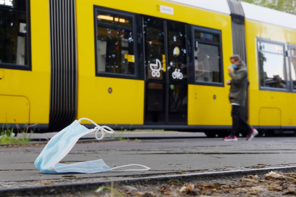 Eine Maske liegt auf dem Boden, dahinter fährt eine Tram: Nur jeder Vierte trägt bei der Fahrt mit den BVG eine Mund-Nase-Bedeckung.