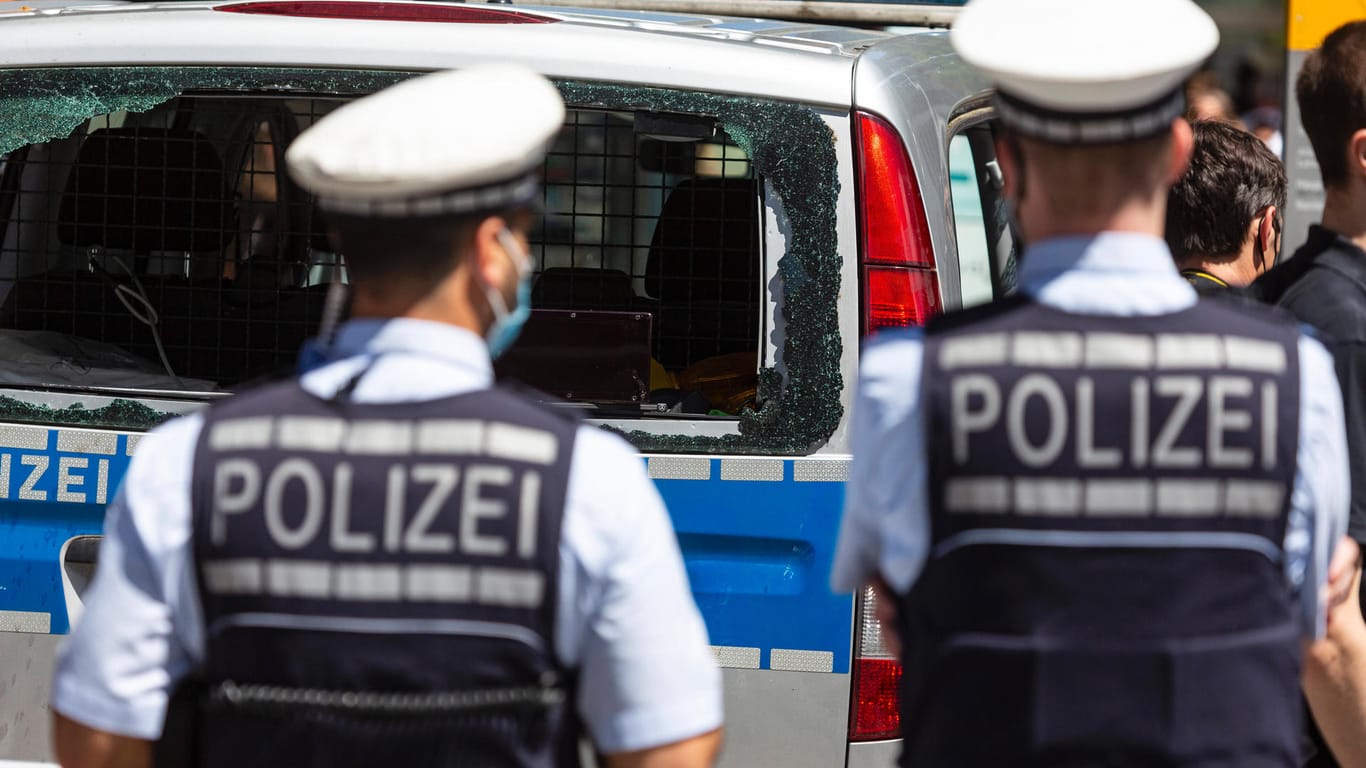 Zwei Polizisten stehen vor einem Einsatzwagen mit zerstörter Scheibe: Nach den Randalen in Stuttgart sitzen mehrere Personen im Gefängnis.