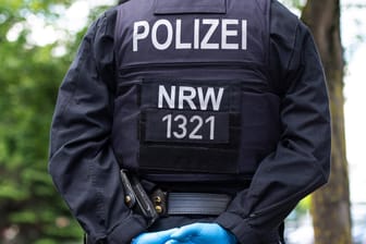 Ein Polizist mit Gummihandschuhen verkreutzt die Hände auf dem Rücken (Symbolbild): In Hagen hat ein Mann seine Ehefrau mit dem Messer bedroht.