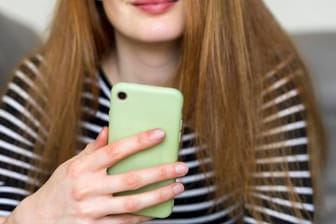 Eine Frau mit Smartphone (Symbolbild): Mit bestimmten Codes können Sie auf Ihrem Handy versteckte Funktionen aktivieren.
