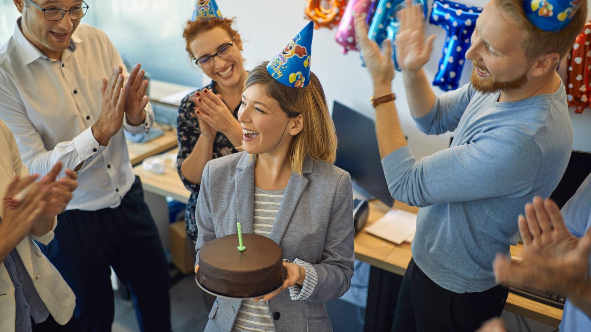 Geburtstagsfeier im Büro: Wer den Kollegen während der Arbeitszeit etwas ausgibt, kann die Kosten dafür von der Steuer absetzen.n in office with cake and party hats model released Symbolfot