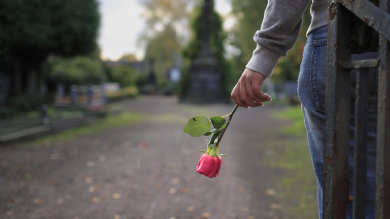 Eine Frau hält eine Rose in der Hand: Beerdigungen gelten steuerlich als außergewöhnliche Belastungen.