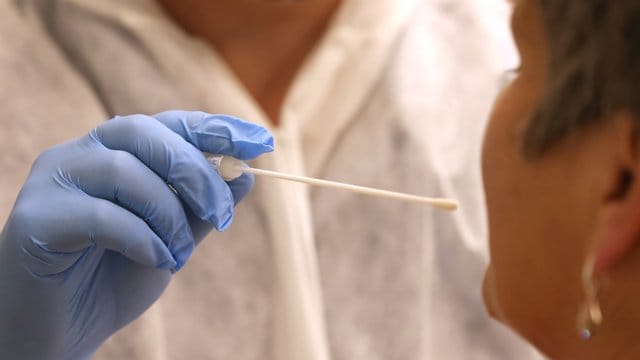 Ein Arzt nimmt in einer Hausarztpraxis mit einem Tupfer einen Abstrich für einen Coronatest. Ein Arzt nimmt in einer Hausarztpraxis mit einem Tupfer einen Abstrich für einen Coronatest.