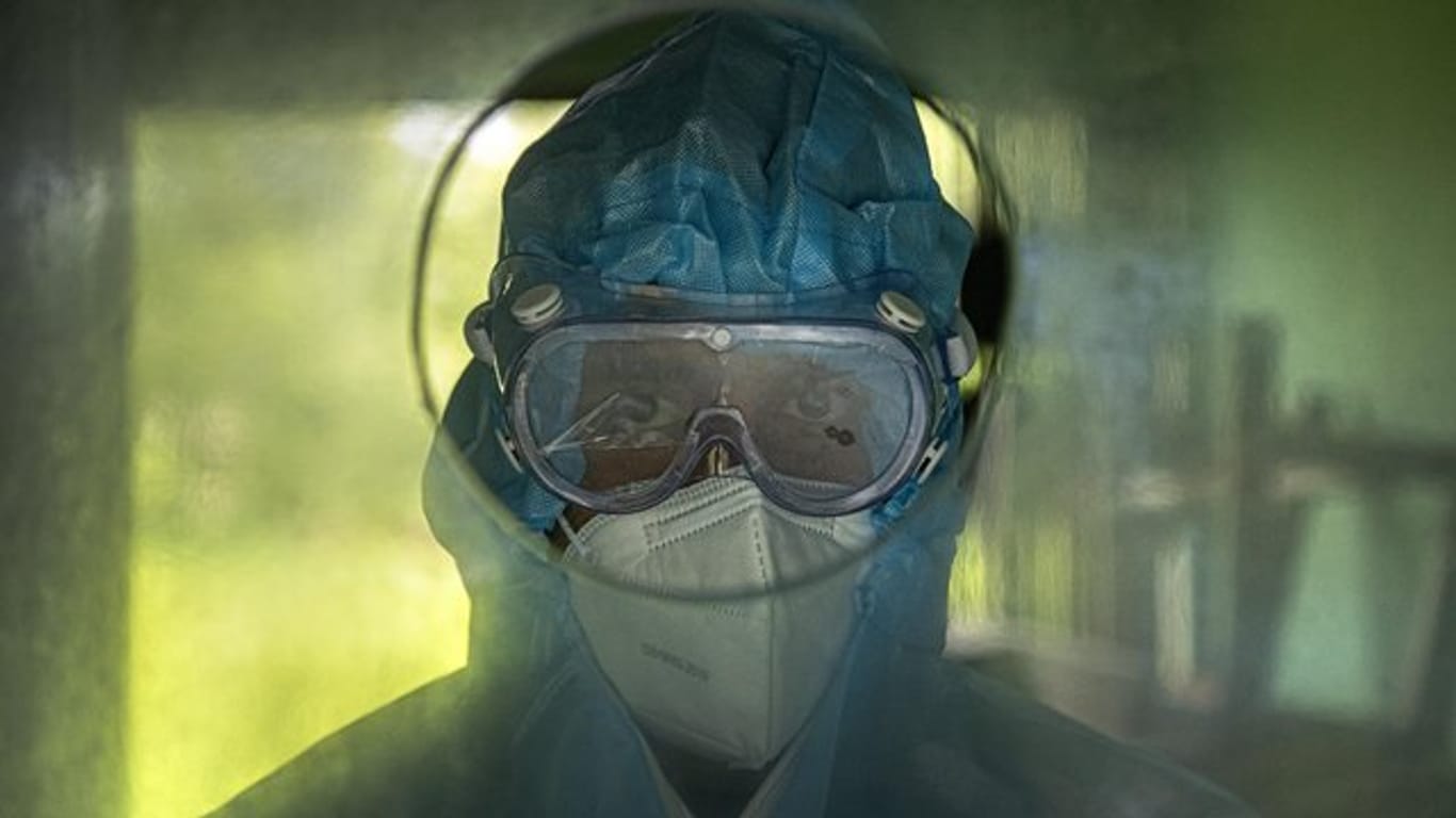Medizinisches Personal wartet hinter einer Glaswand darauf, Patienten Nasenabstriche zu entnehmen.