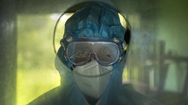 Medizinisches Personal wartet hinter einer Glaswand darauf, Patienten Nasenabstriche zu entnehmen. Medizinisches Personal wartet hinter einer Glaswand darauf, Patienten Nasenabstriche zu entnehmen.