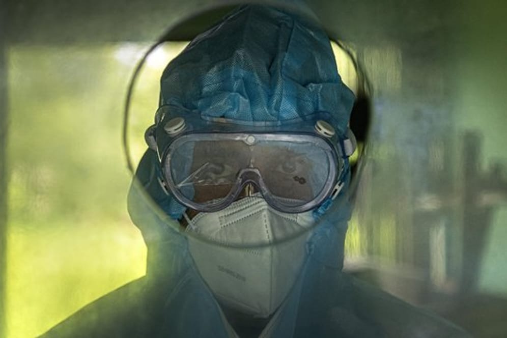 Medizinisches Personal wartet hinter einer Glaswand darauf, Patienten Nasenabstriche zu entnehmen.