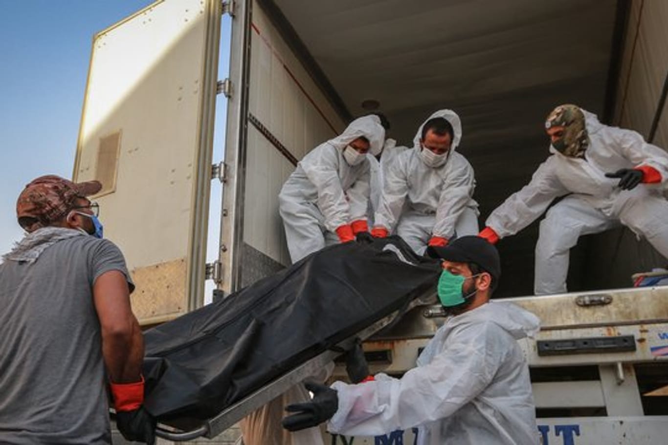 Arbeiter in Schutzkleidung beladen in Bagdad einen Kühlwagen mit Leichen von Menschen, die am Coronavirus gestorben sind.