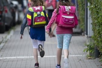 Zwei Schülerinnen einer Grundschule rennen mit einem Schulranzen auf dem Rücken die letzten Meter bis zum Schulhof.